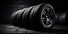 New Tires Pile On A Dark Black Background. Tire Fitting Background With Stack Of Car Tires. Copy Space. 