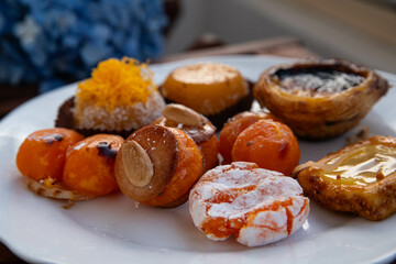 Mix of traditional Portuguese egg yolk sweets from Porto region on white plate with blue hydrangea on background.