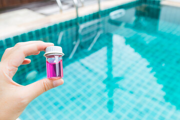 Wall Mural - Glass vials in girl hand over blurred swimming pool background, outdoor day light, pH test