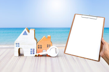 Wall Mural - Miniature wooden house with key and blank clipboard over tropical beach background, property report, real estate business and investment