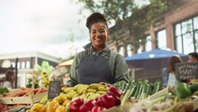 Portrait Of A Black Female Working At A Farmers Market Stall With Fresh Organic Agricultural Products. Businesswoman Looking At Camera And Smiling. African Farmer Selling Eco Fruits And Vegetables