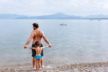 Wall Mural - rear view on father holding the hand of little daughter on the beach