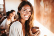 © Jasmina - Portrait of a happy and smiling yoga teacher on Ibiza island, holding cacao drink in ceramic cup. Blurred people in the background