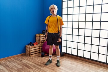 Canvas Print - Young man training arm resistance with elastic arm bands afraid and shocked with surprise and amazed expression, fear and excited face.