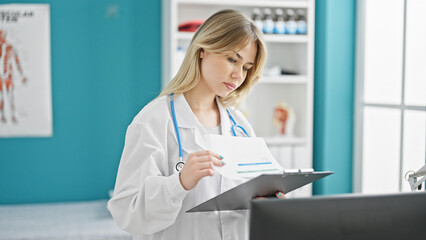 Poster - Young blonde woman doctor reading document on clipboard at clinic