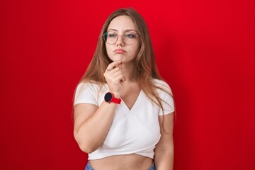 Sticker - Young caucasian woman standing over red background thinking concentrated about doubt with finger on chin and looking up wondering