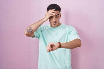 Poster - Handsome hispanic man standing over pink background looking at the watch time worried, afraid of getting late