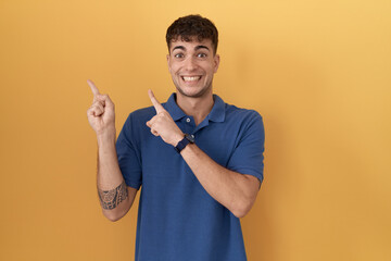 Sticker - Young hispanic man standing over yellow background pointing aside worried and nervous with both hands, concerned and surprised expression