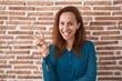 © Krakenimages.com - Brunette woman standing over bricks wall smiling with happy face winking at the camera doing victory sign. number two.