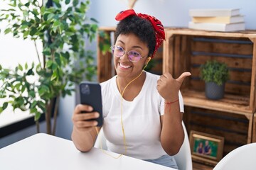 Poster - Young african american woman doing video call with smartphone pointing thumb up to the side smiling happy with open mouth