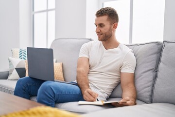 Sticker - Young caucasian man using laptop writing on notebook at home