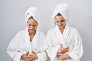 Poster - Middle age woman and daughter wearing white bathrobe and towel with hand on stomach because nausea, painful disease feeling unwell. ache concept.