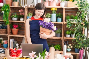 Canvas Print - Young caucasian woman florist using laptop holding plant at florist