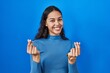 © Krakenimages.com - Young brazilian woman standing over blue isolated background doing money gesture with hands, asking for salary payment, millionaire business