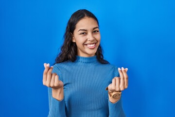 Poster - Young brazilian woman standing over blue isolated background doing money gesture with hands, asking for salary payment, millionaire business