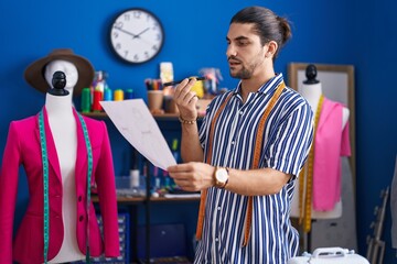 Sticker - Young hispanic man tailor talking on smartphone reading document at sewing studio