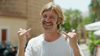 Poster - Young blond man smiling confident doing surf sign with fingers at street