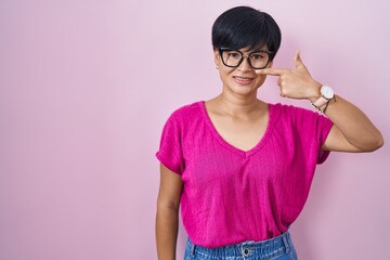 Canvas Print - Young asian woman with short hair standing over pink background pointing with hand finger to face and nose, smiling cheerful. beauty concept