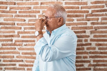 Sticker - Senior man with grey hair standing over bricks wall tired rubbing nose and eyes feeling fatigue and headache. stress and frustration concept.