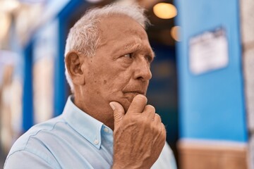 Wall Mural - Senior grey-haired man standing with doubt expression at street