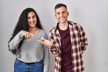 Sticker - Young hispanic couple standing over white background amazed and smiling to the camera while presenting with hand and pointing with finger.