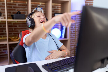 Poster - Young caucasian woman playing video games wearing headphones laughing at you, pointing finger to the camera with hand over body, shame expression