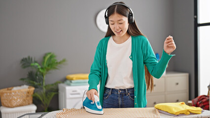 Poster - Young chinese woman listening to music ironing clothes dancing at laundry room