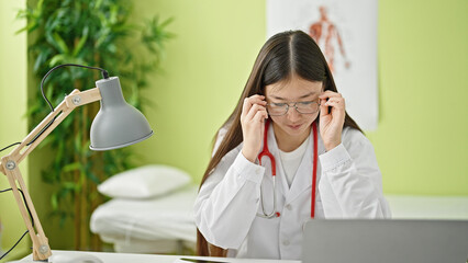 Young chinese woman doctor using laptop wearing glasses at clinic