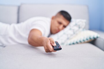 Canvas Print - Young latin man watching tv lying on sofa at home