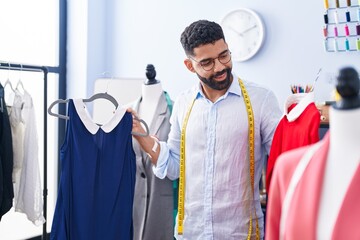 Sticker - Young arab man tailor smiling confident holding t shirts at tailor shop