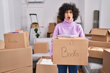 Sticker - Young brunette woman with curly hair moving to a new home holding cardboard box angry and mad screaming frustrated and furious, shouting with anger. rage and aggressive concept.