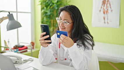 Wall Mural - Young chinese woman doctor shopping with smartphone and credit card at the clinic