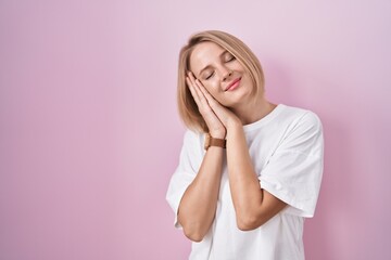 Canvas Print - Young caucasian woman standing over pink background sleeping tired dreaming and posing with hands together while smiling with closed eyes.