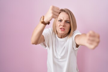 Canvas Print - Young caucasian woman standing over pink background angry and mad raising fists frustrated and furious while shouting with anger. rage and aggressive concept.