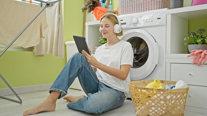 Wall Mural - Young blonde woman listening to music sitting on floor at laundry room
