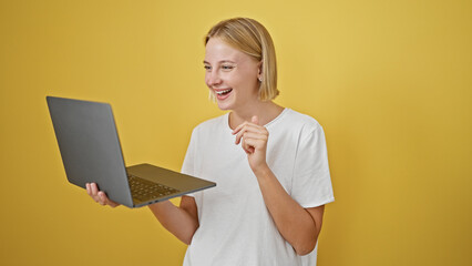 Poster - Young blonde woman using laptop smiling over isolated yellow background