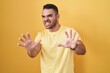 © Krakenimages.com - Young hispanic man standing over yellow background afraid and terrified with fear expression stop gesture with hands, shouting in shock. panic concept.
