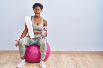 Sticker - African american woman wearing sportswear sitting on pilates ball angry and mad screaming frustrated and furious, shouting with anger. rage and aggressive concept.