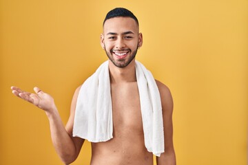 Canvas Print - Young hispanic man standing shirtless with towel smiling cheerful presenting and pointing with palm of hand looking at the camera.