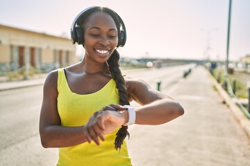 Wall Mural - African american woman listening to music looking stopwatch at street