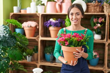 Sticker - Young hispanic woman working at florist shop holding plant looking positive and happy standing and smiling with a confident smile showing teeth