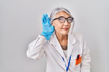 Poster - Middle age woman with grey hair wearing scientist robe smiling with hand over ear listening an hearing to rumor or gossip. deafness concept.