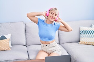 Poster - Young blonde woman dancing and listening to music sitting on sofa at home