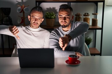 Canvas Print - Homosexual couple using computer laptop looking unhappy and angry showing rejection and negative with thumbs down gesture. bad expression.