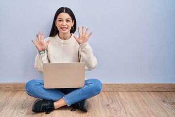 Sticker - Young woman using laptop sitting on the floor at home showing and pointing up with fingers number ten while smiling confident and happy.