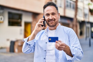 Poster - Young caucasian man talking on smartphone holding credit card at street