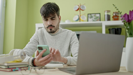 Poster - Young hispanic man student using smartphone at dinning room