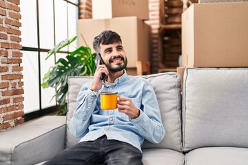 Wall Mural - Young hispanic man talking on smartphone drinking coffee at new home