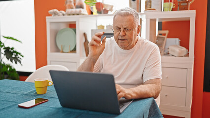 Wall Mural - Middle age grey-haired man having video call sitting on table at dinning room