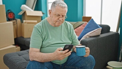 Wall Mural - Middle age grey-haired man using smartphone drinking coffee at new home